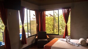 A hotel room with a bed, a chair, and large windows with curtains. - Cabañas Colibrí Tayutic (Tayutic)