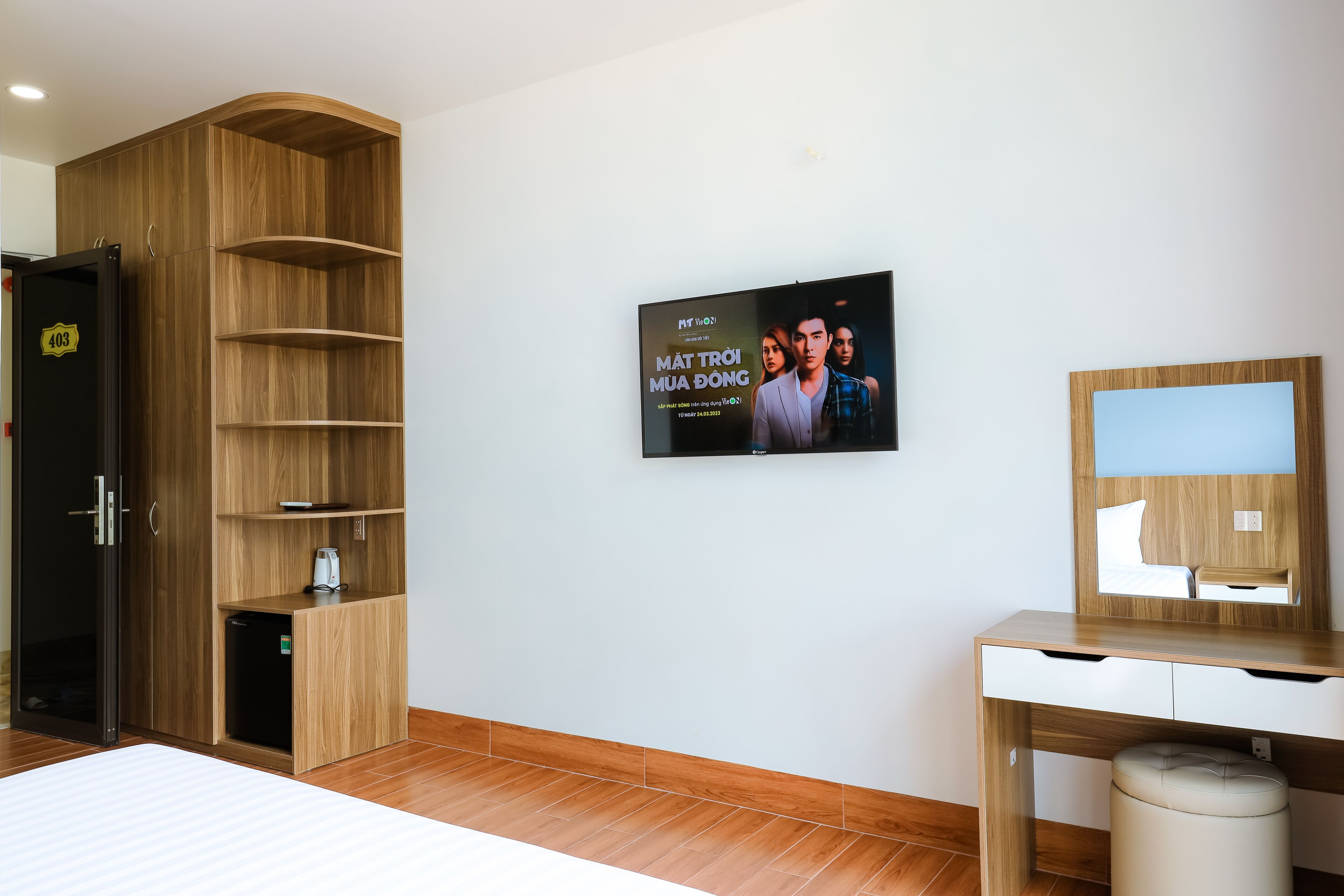 Habitación de hotel con un armario de madera, un escritorio con espejo y un televisor de pared mostrando un cartel de película.