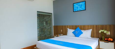 A modern hotel room with a wooden bed, a blue accent runner, a nightstand with a vase of flowers, and a wall-mounted air conditioner.