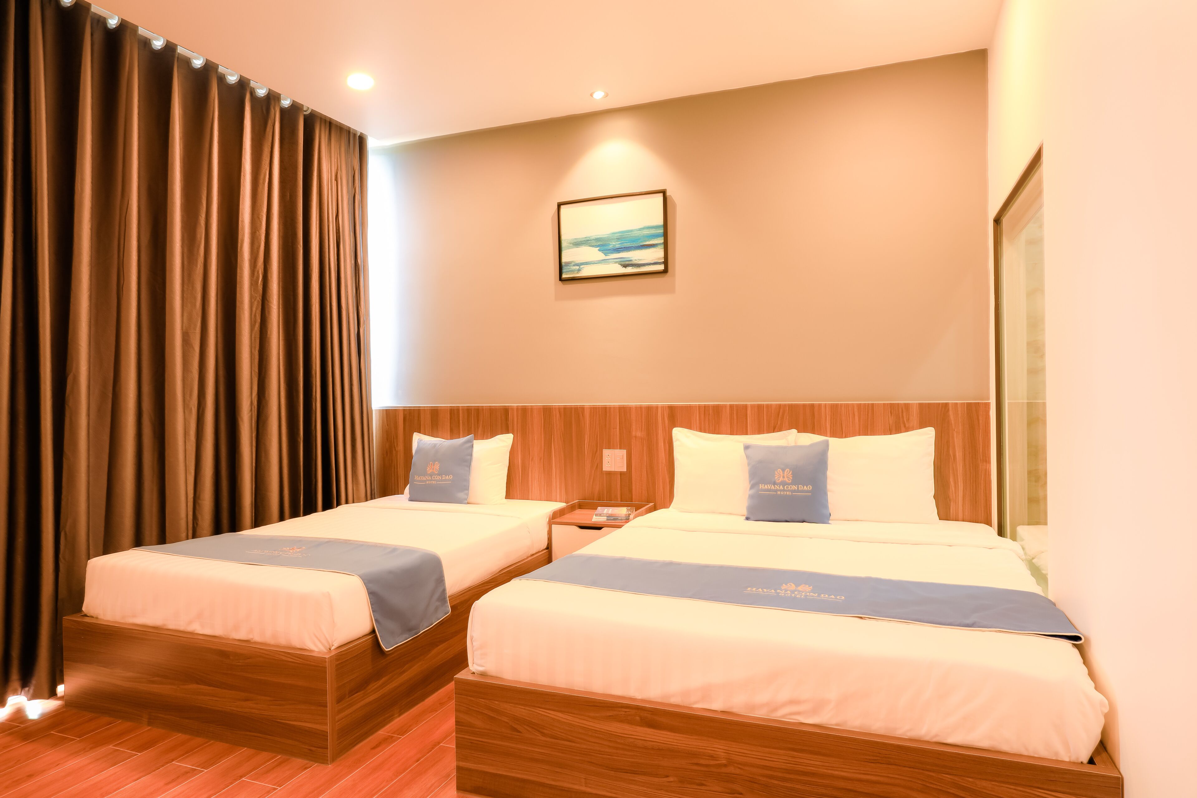 Habitación de hotel con dos camas, cabeceros de madera, una mesita de noche y un cuadro en la pared.