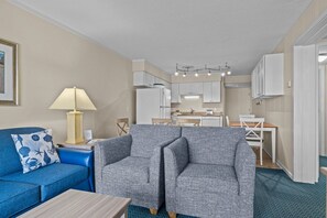 A modern living room with a blue sofa, a grey armchair, a wooden coffee table, and a lamp.