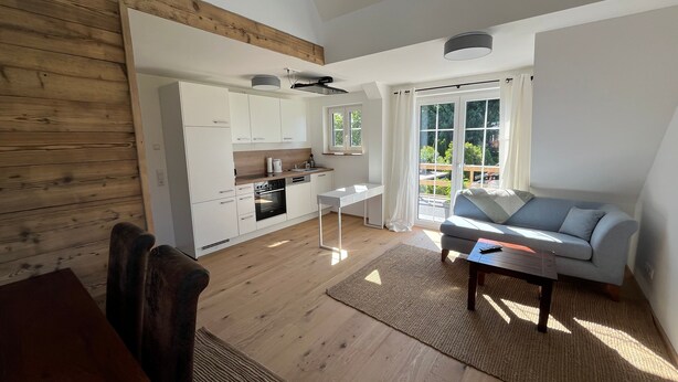 Een moderne keuken met witte kasten, een eethoek met tafel en stoelen, en een woonkamer met een bank en salontafel.