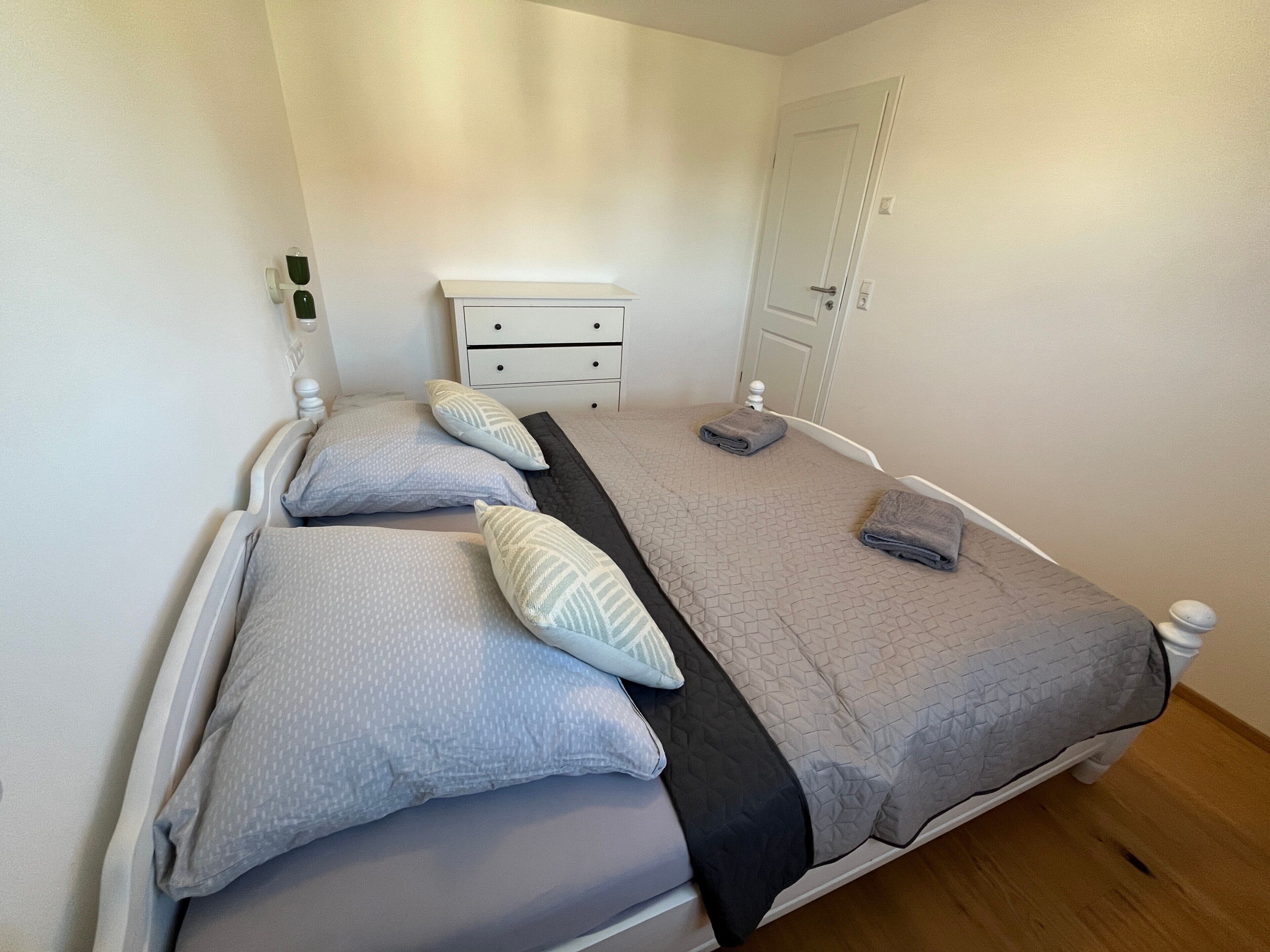 Un letto rifatto con cuscini e coperta, un comodino con una lampada e una porta sullo sfondo.