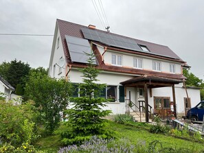 Ein Haus mit geneigtem Dach, Solaranlagen, einer Veranda und einem Garten mit verschiedenen Pflanzen.