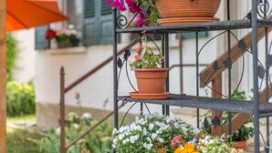 Een metalen plantenstandaard buiten met terracotta potten met bloemen.