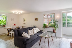 Un salon comprenant un canapé, une table basse en verre, une table à manger avec des chaises et des plantes en pot.