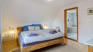 Un dormitorio con una cama de madera, una mesita de noche con lámpara, un espejo y una puerta que da a un baño.