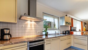 A modern kitchen with a stove, oven, and sink, a window with curtains, and a countertop with a coffee maker. - Apartment 'Im Rosengarten' with Mountain View, Private Terrace and Wi-Fi (Zell am Harmersbach)