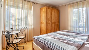A bedroom with a bed, a wooden wardrobe, a round table with chairs, and sheer curtains. - Apartment 'Im Rosengarten' with Mountain View, Private Terrace and Wi-Fi (Zell am Harmersbach)