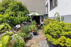 Ein Garten mit Topfpflanzen, einer Terrassenfläche und einem Gebäude mit weißer Fassade.