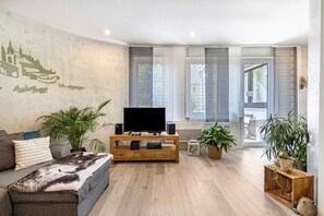 A living room with a flat-screen TV on a wooden TV stand, a sofa, and potted plants. - Premium Apartment 'Für Traufgängerle' with Private Terrace, Garden & Infrared Cabin (Albstadt)