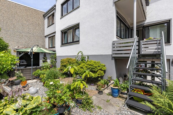 A residential building with a balcony, a small garden area with potted plants, and a metal staircase. - Premium Apartment 'Für Traufgängerle' with Private Terrace, Garden & Infrared Cabin (Albstadt)