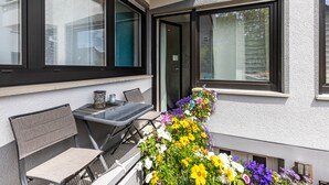 A balcony with a table and chairs, a flower arrangement, and large windows. - Premium Apartment 'Für Traufgängerle' with Private Terrace, Garden & Infrared Cabin (Albstadt)