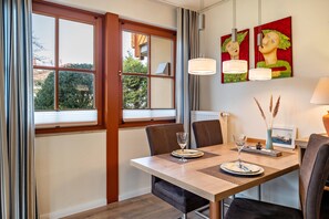 Un comedor con una mesa dispuesta para dos personas, una ventana con persianas y dos lámparas colgantes fijadas a la pared.
