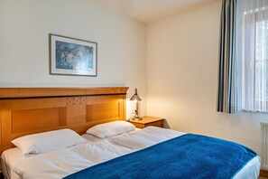 Habitación de hotel con cama, mesita de noche, lámpara, un cuadro en la pared y una ventana con cortinas.