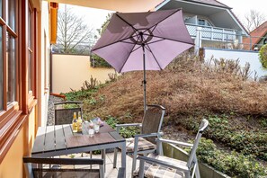 Un patio exterior con una mesa, sillas y un paraguas morado.