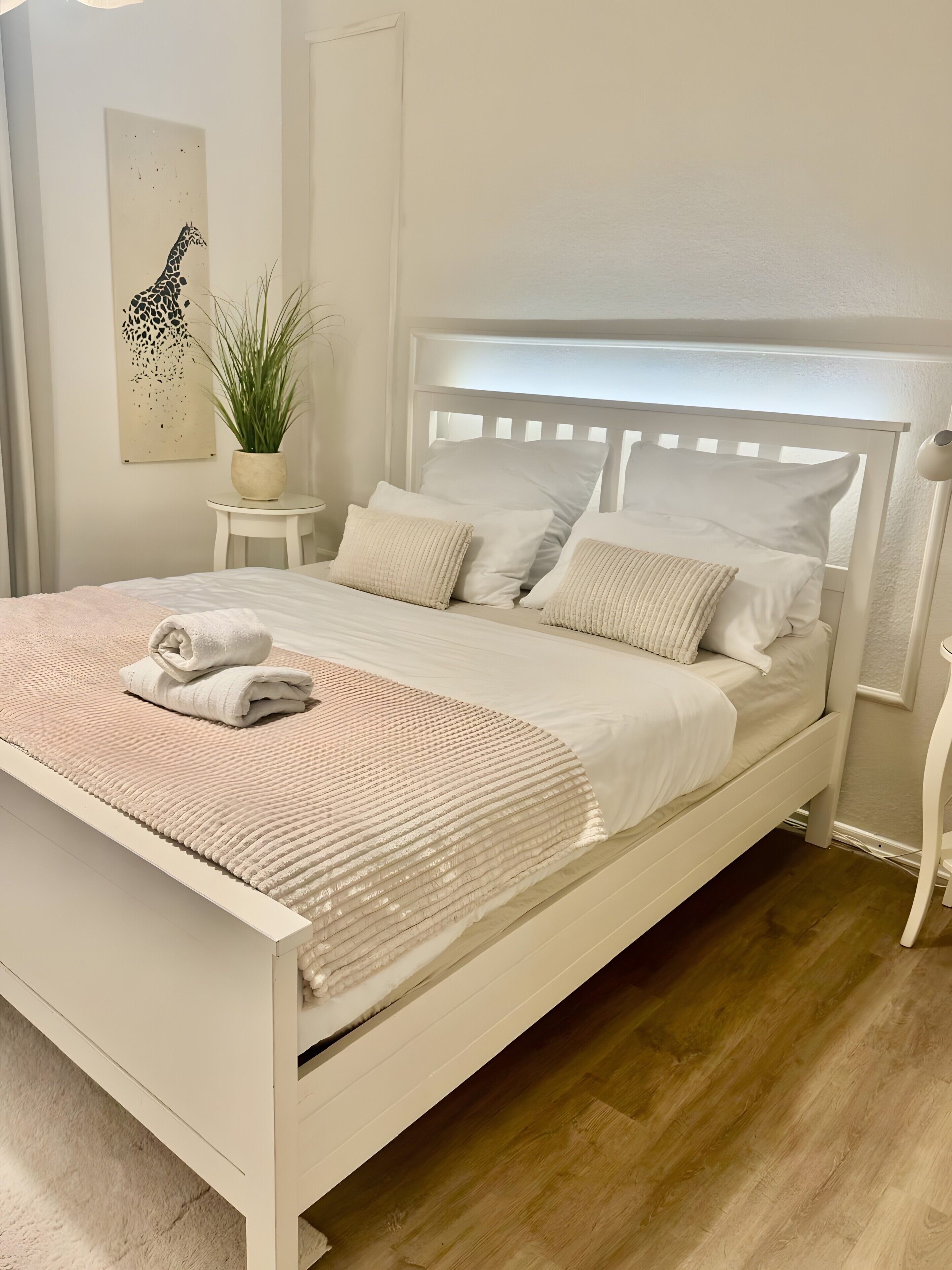 A white bed with a headboard, white pillows, and a folded towel on the bed.