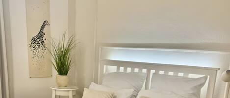 A white bed with a headboard, white pillows, and a folded towel on the bed.