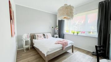 A bedroom with a bed, bedside tables, a chair, a window with curtains, and a hanging light fixture.