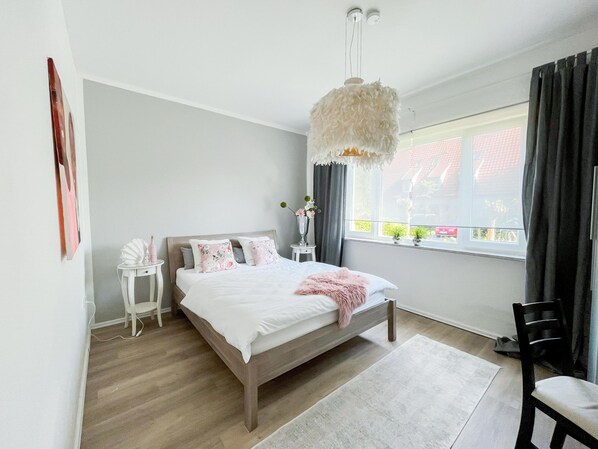 Une chambre à coucher comprenant un lit, des tables de chevet, une chaise, une fenêtre avec des rideaux et un luminaire suspendu.