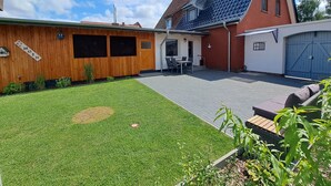 En boligejendom med en velplejet græsplæne, en patio med udendørs møbler, og en bygning med rødt tag.