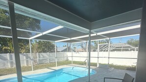 Una piscina exterior techada con cerramiento de vidrio, una mesa y dos sillas.