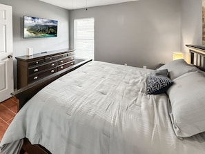 Quarto com cama, penteadeira e televisão na parede.