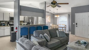Una sala moderna con un sofá gris, una mesa de centro y una zona de comedor con sillas azules.