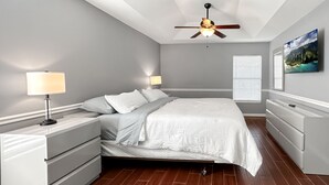 Un dormitorio con cama, mesitas de noche, cómoda, ventilador de techo y ventana con persianas.