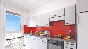 A modern kitchen with white cabinets, a red tiled backsplash, a built-in oven, and two bar stools.