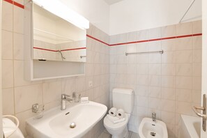 Une salle de bain équipée d’un lavabo, d’un miroir, de toilettes, d’un bidet et d’un porte-serviettes.
