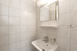 Une salle de bain avec des carreaux blancs, un lavabo, un miroir et un porte-serviettes.