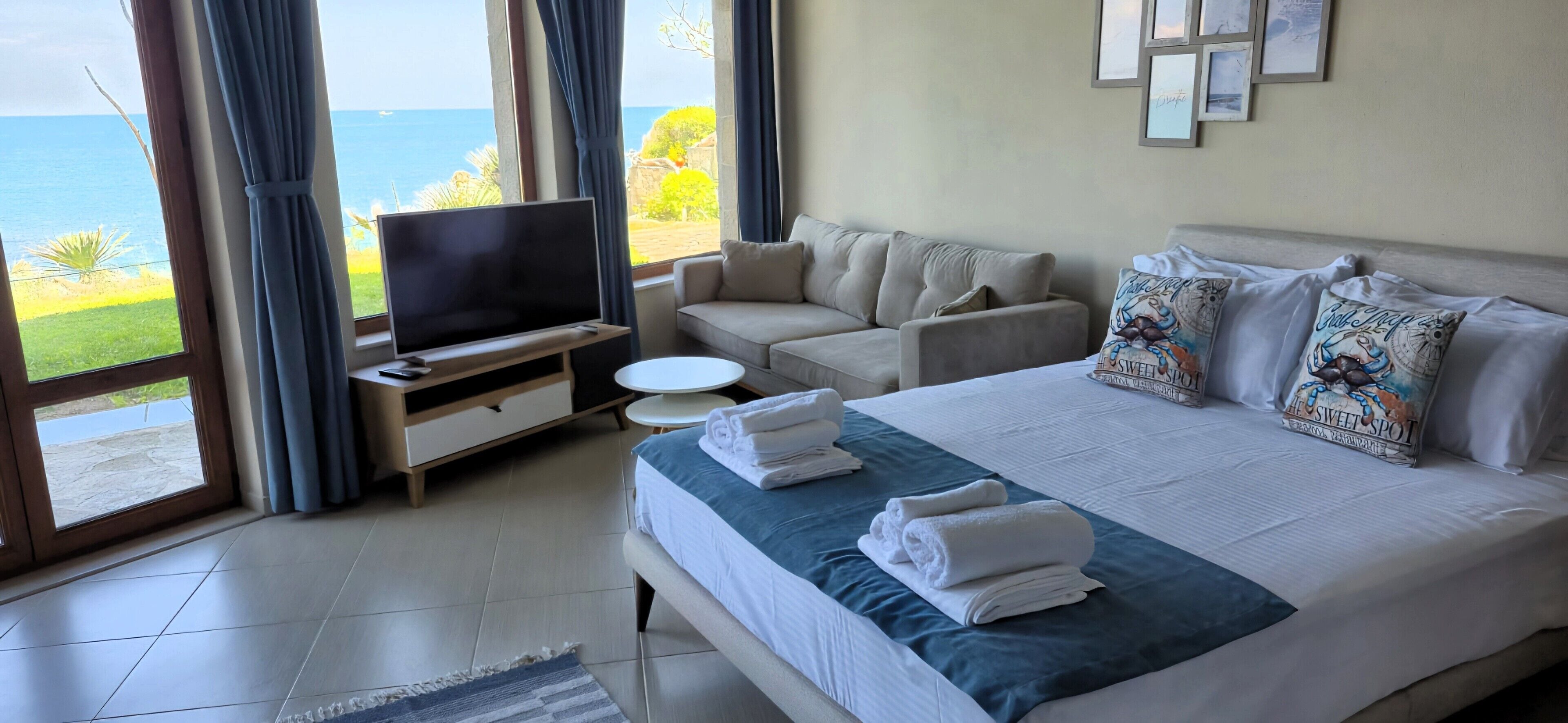 A hotel room with a large bed, a TV, a sofa, and a view of the sea.
