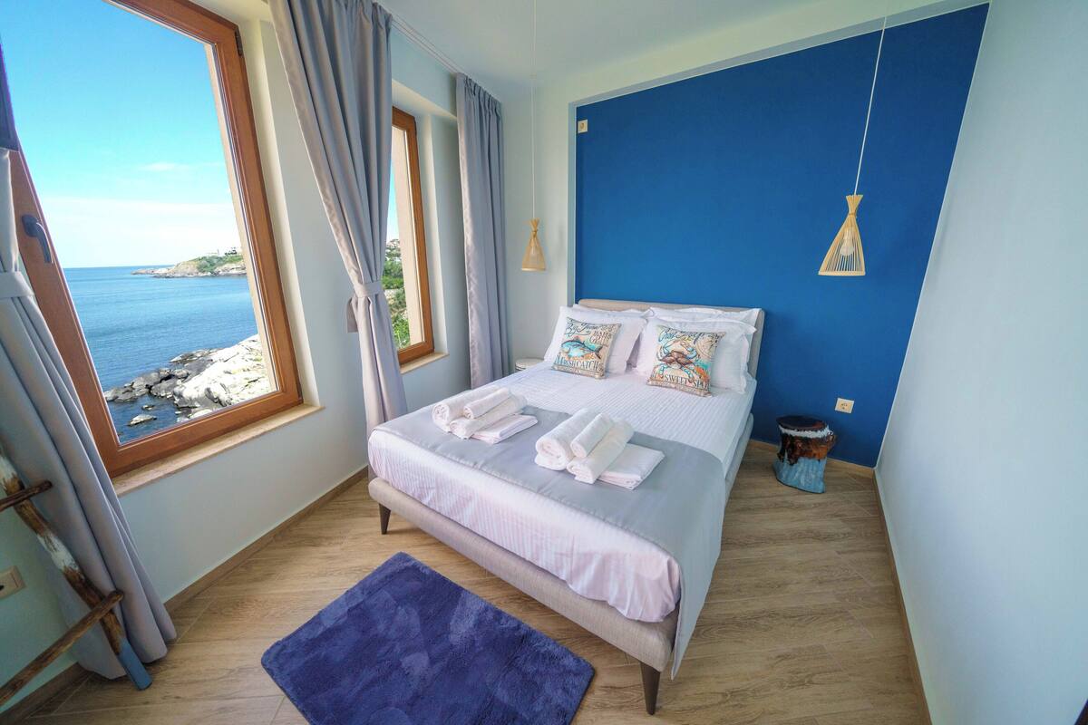 Une chambre avec une grande fenêtre, un lit sur lequel sont soigneusement pliées des serviettes, et un mur bleu.