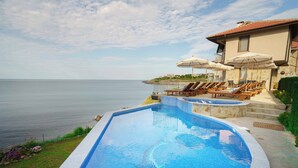 Piscina con sillas de descanso y sombrillas, con vista a una extensión de agua.