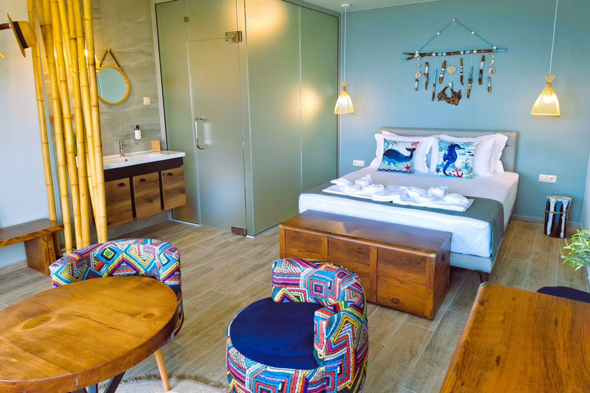 Une chambre à coucher moderne avec un lit, une table de chevet et une petite chaise en bois. On y trouve également une salle de bain avec un lavabo et un miroir.