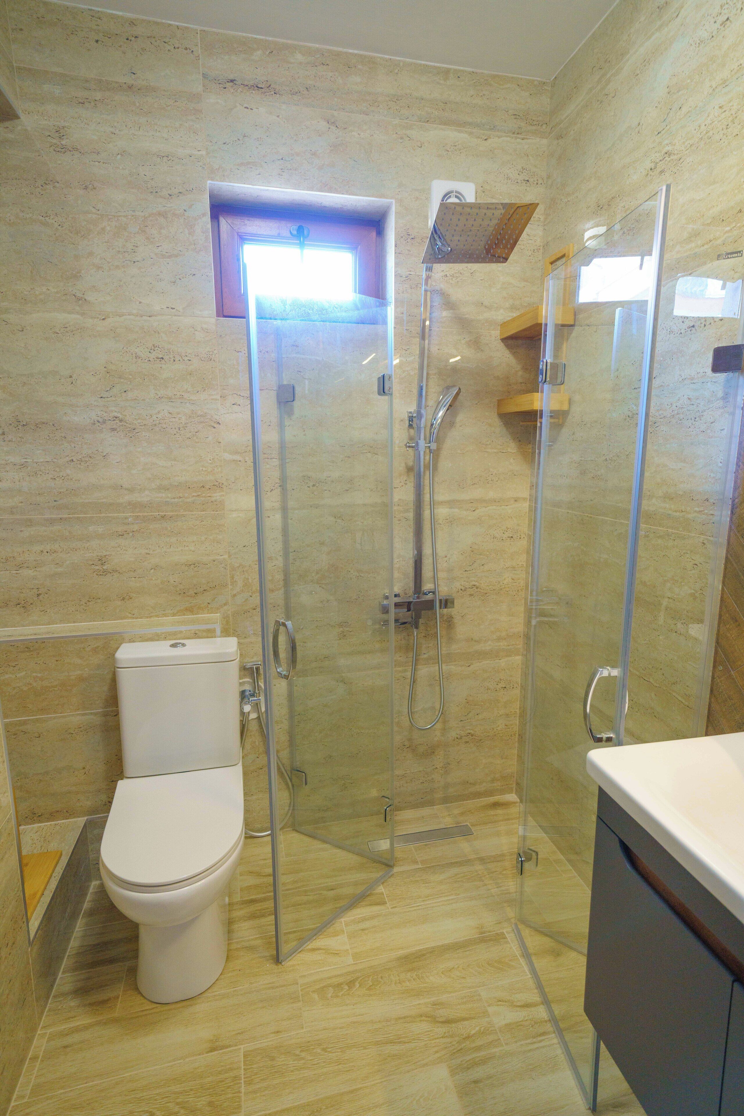 Un bany modern amb plat de dutxa envoltat de vidre, un vàter i un lavabo amb mirall.