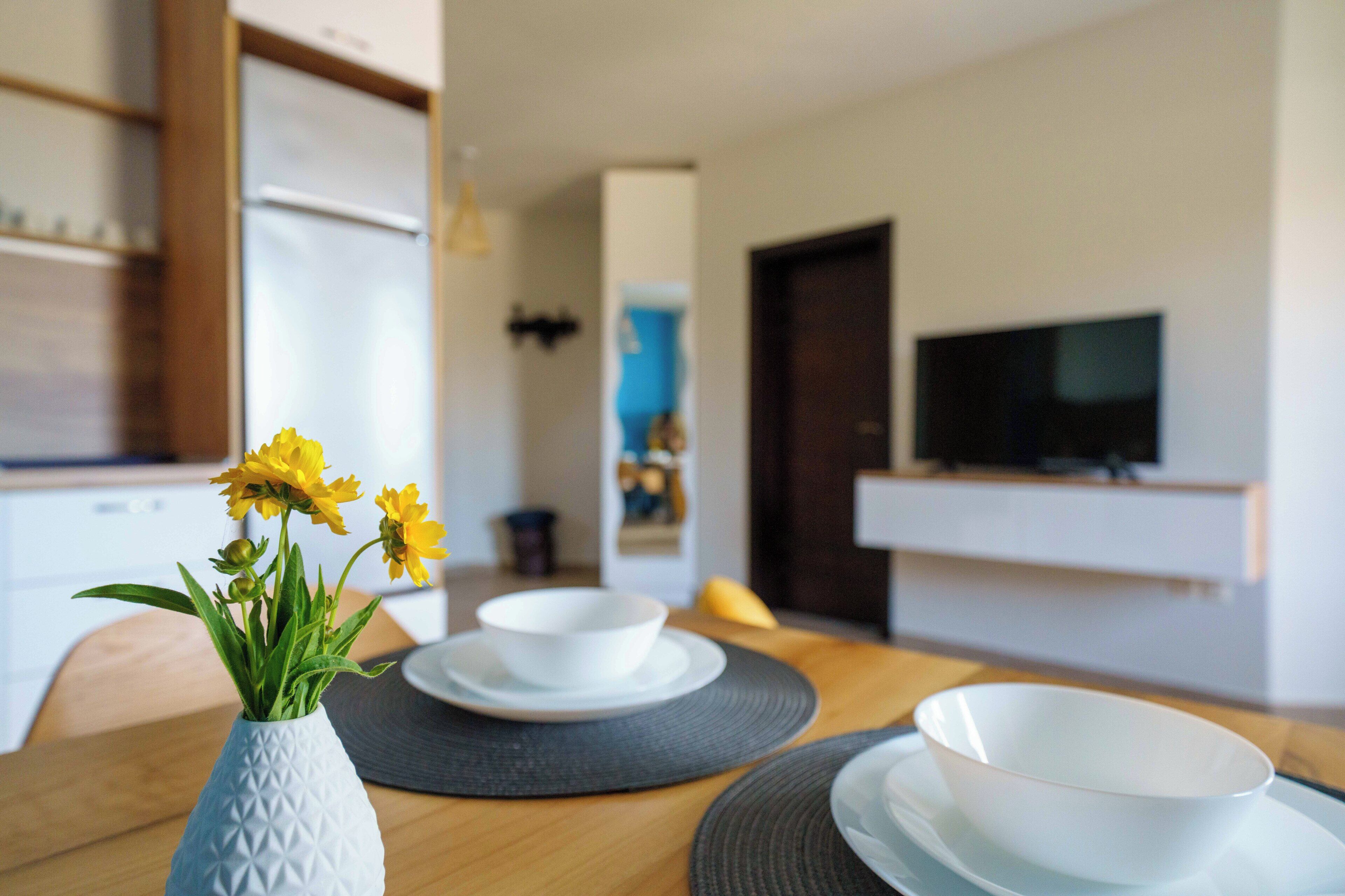 Ein Essbereich mit einem Holztisch, weißen Schüsseln und einer Vase mit gelben Blumen.