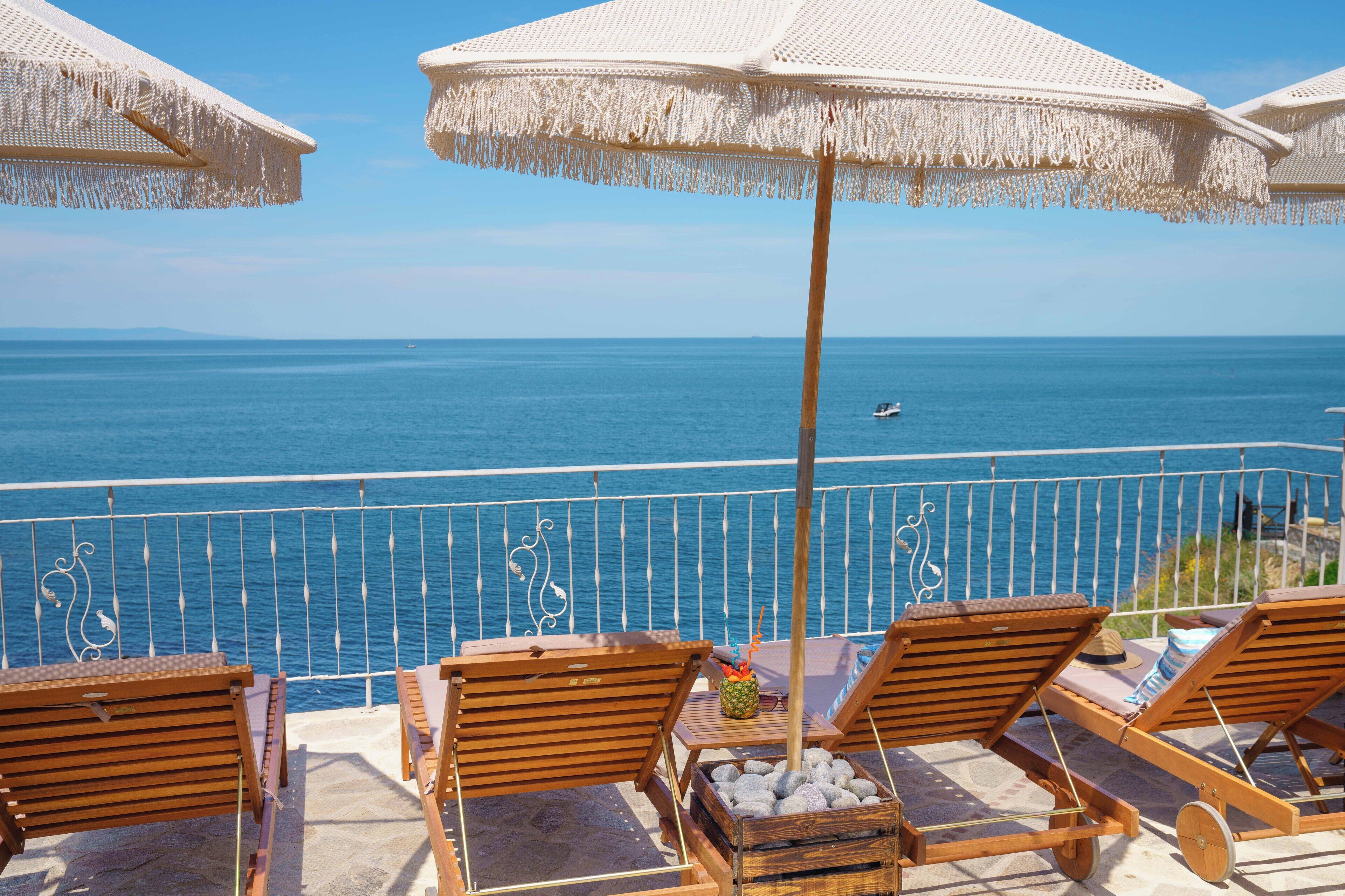 Un balcon doté de chaises longues en bois et de parasols blancs, offrant une vue sur la mer.