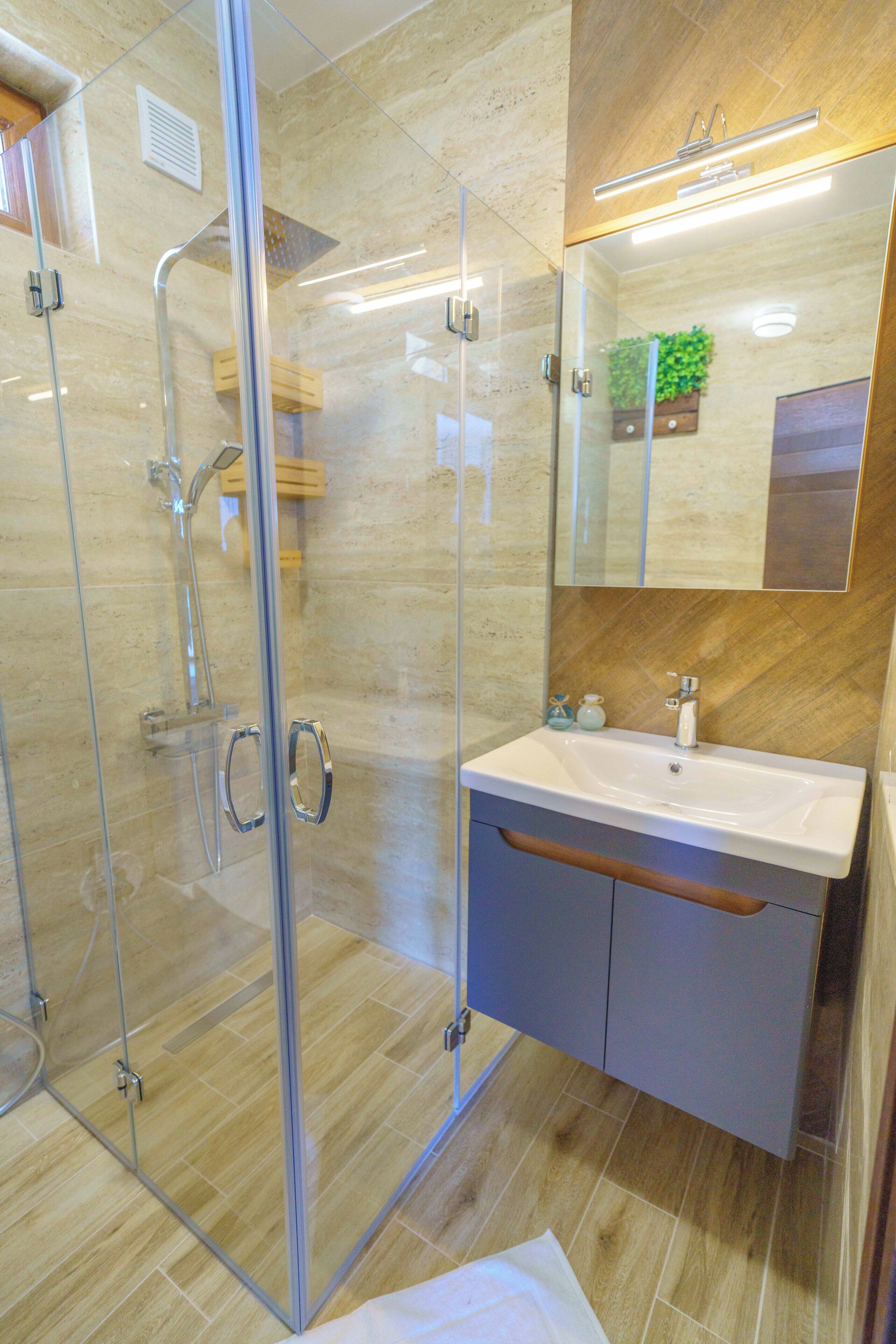 Ein modernes Badezimmer mit einer Glaskabine zur Dusche, einem weißen Waschbecken und einem Spiegel darüber.