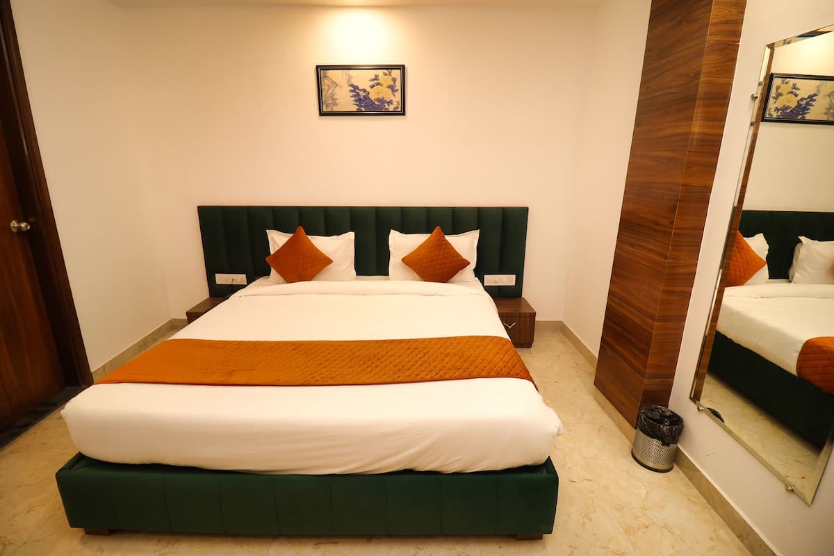 Una cama bien hecha con cabecera verde, ropa de cama blanca y detalles en naranja.