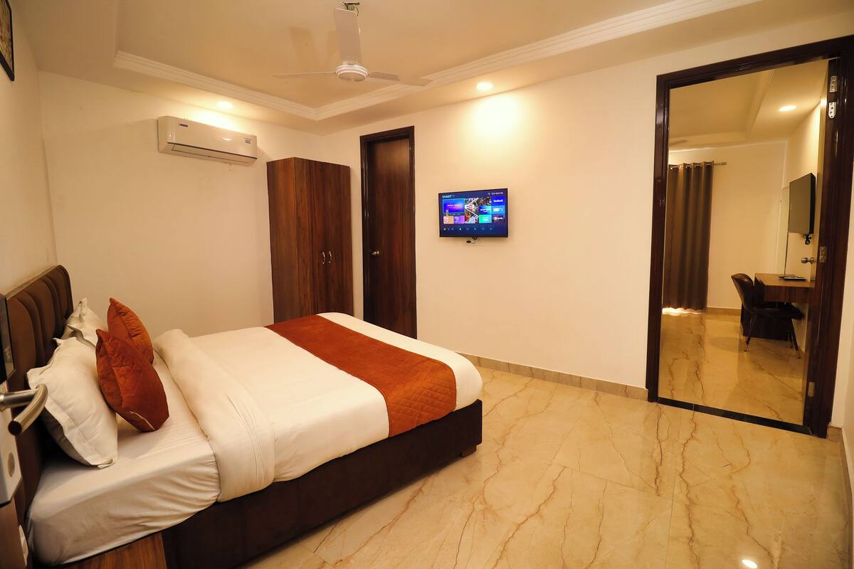 Habitación de hotel con cama, televisor, armario y baño visible a través de una puerta de cristal.