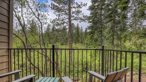 Une terrasse en bois avec deux chaises et une table, entourée d’une rambarde en métal, donnant sur une zone boisée.