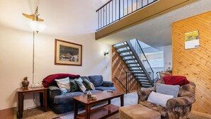 Un salon comprenant un canapé, un fauteuil, une table basse et un escalier menant à l’étage supérieur.