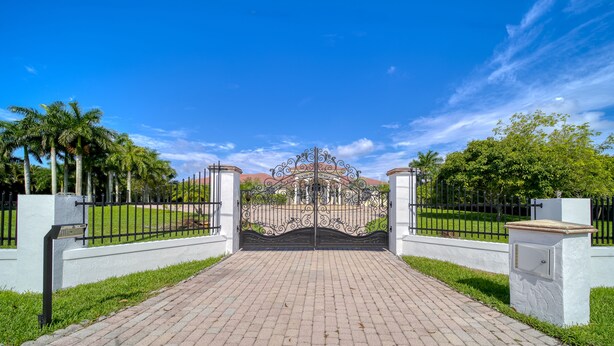 A paved pathway leading to a gated entrance with a decorative iron gate.