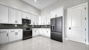 A modern kitchen with white cabinets, a black refrigerator, a microwave, and a stove.