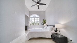 A bedroom with a bed, bedside table, lamp, and a ceiling fan.
