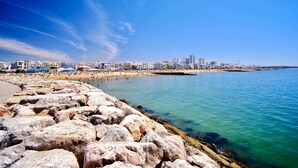 Un paisaje urbano costero con un litoral rocoso, una playa arenosa y una hilera de edificios a la orilla del agua.