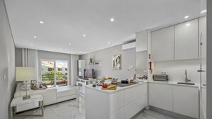 Una cocina moderna con armarios blancos, una isla central y un comedor con sofá y mesa.