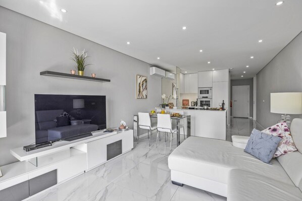 Una sala de estar moderna con un televisor de pantalla plana grande, un sofá, un comedor y una cocina al fondo.